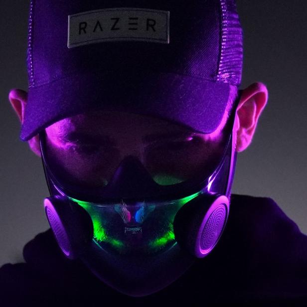 Eine Person trägt eine leuchtende „Razer“-Maske und eine Kappe.