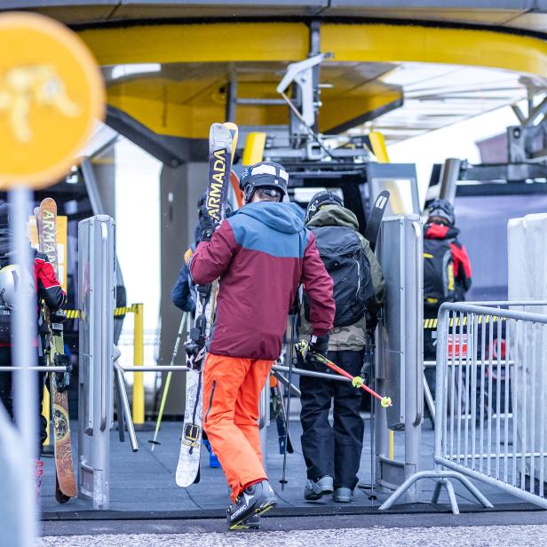 Skifahrer gehen durch eine Drehkreuzanlage, um einen Skilift zu benutzen.