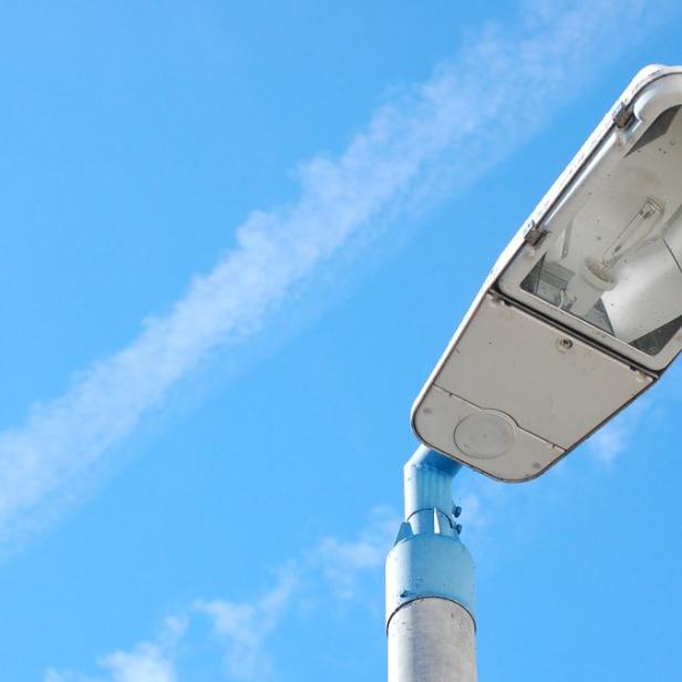 Eine Straßenlaterne vor einem hellblauen Himmel mit Kondensstreifen.