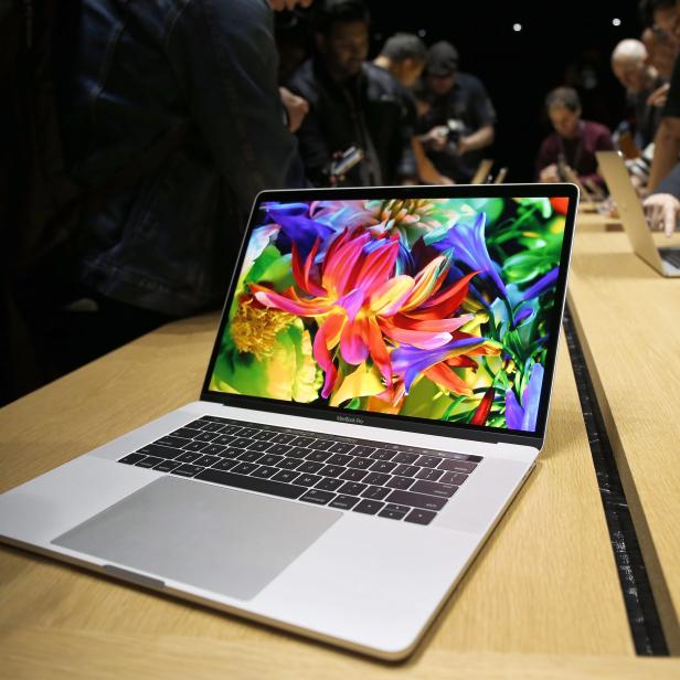 Ein MacBook Pro mit einem farbenfrohen Blumenbild auf dem Bildschirm steht auf einem Holztisch.