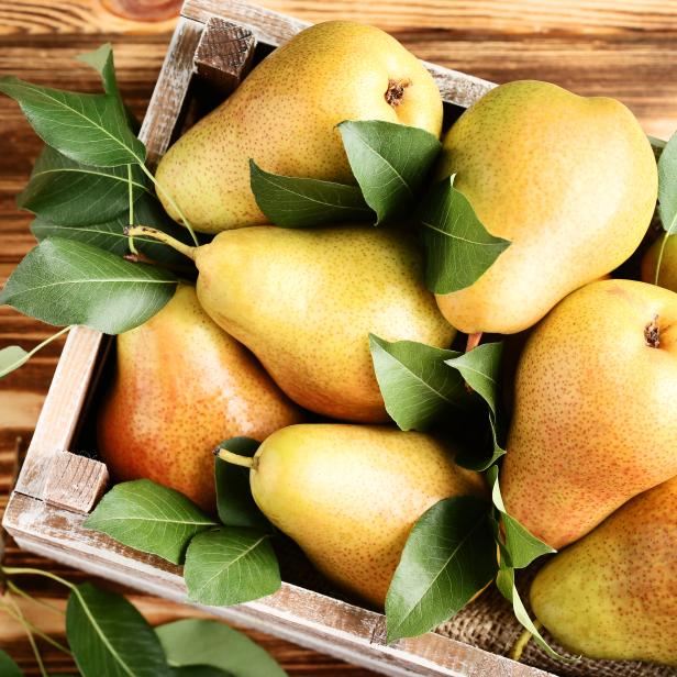 Ripe pears and green leafs in crate on brown wooden table