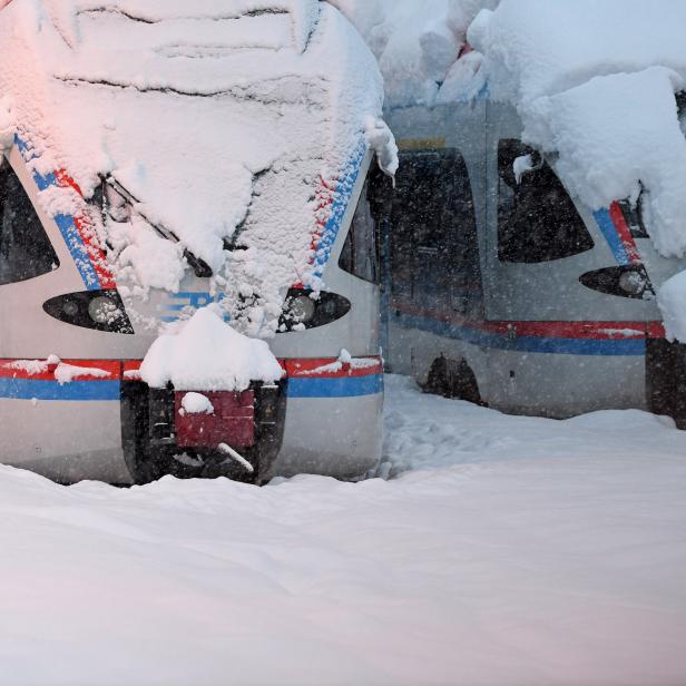 Two regional trains that are covered with snow stand at the train station in Berchtesgaden