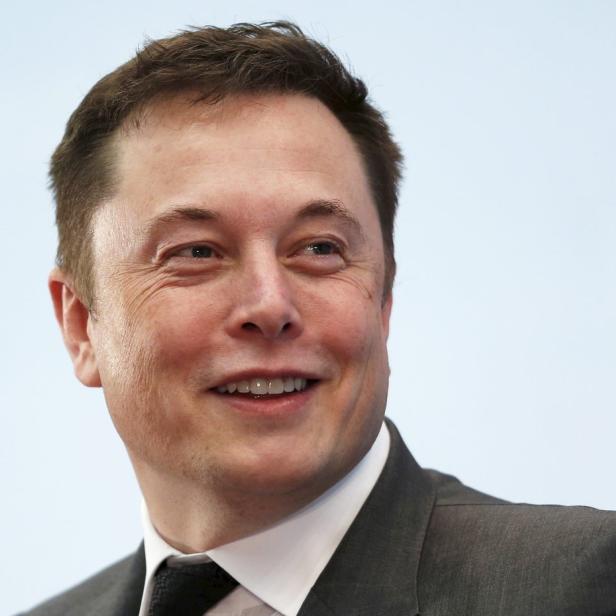 Ein Porträt von Elon Musk, der lächelt und einen dunklen Anzug trägt.