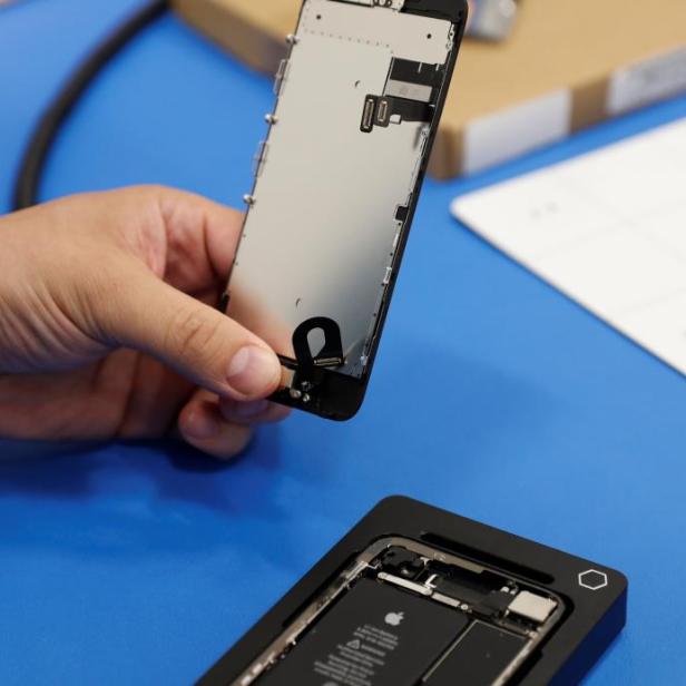 Eine Hand hält ein teilweise demontiertes iPhone über einem Reparaturset.