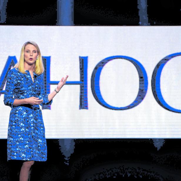 Eine Frau in einem blauen Kleid steht vor einem großen „Yahoo!“-Logo.