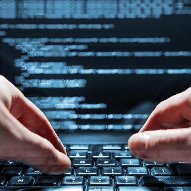 Eine Person tippt auf einer Laptop-Tastatur vor einem Bildschirm mit Code.