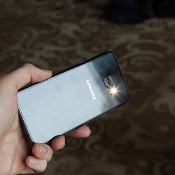 Eine Hand hält ein schwarzes Samsung-Smartphone mit eingeschalteter Taschenlampe.