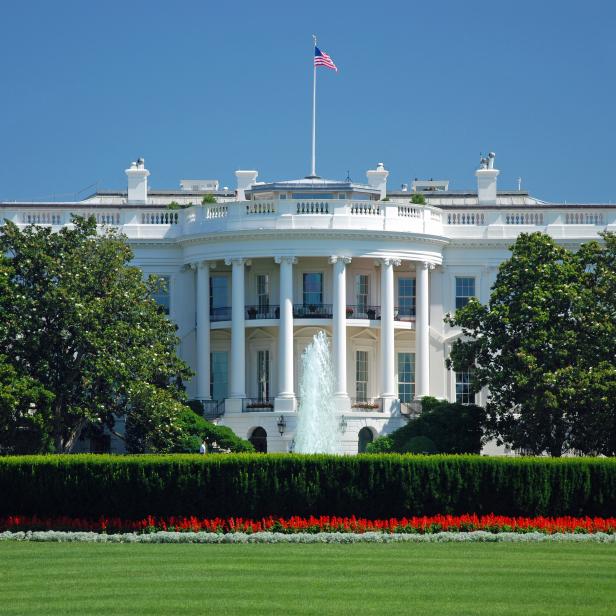 Das Weiße Haus mit amerikanischer Flagge unter blauem Himmel.