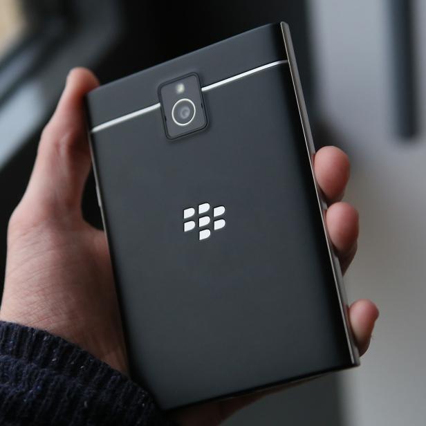 Eine Hand hält ein schwarzes Blackberry-Smartphone mit silbernen Akzenten.