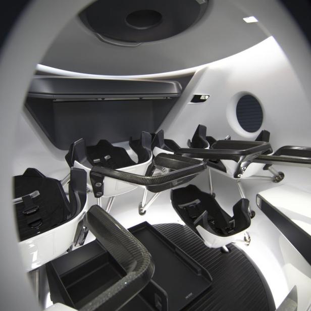 Innenansicht eines Raumschiffs mit mehreren Sitzen und einem kleinen Fenster.