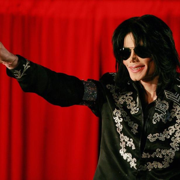Michael Jackson in einer schwarzen Jacke mit silbernen Verzierungen vor einem roten Vorhang.