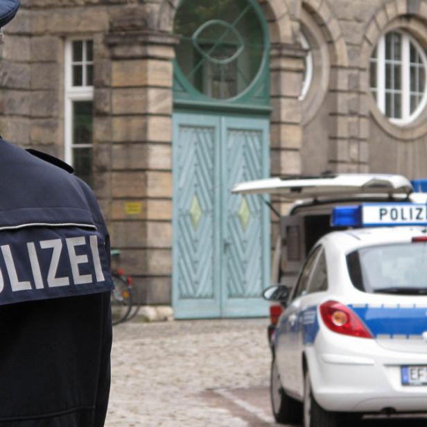 Ein Polizist steht vor einem Gebäude, im Hintergrund parken Polizeiautos.