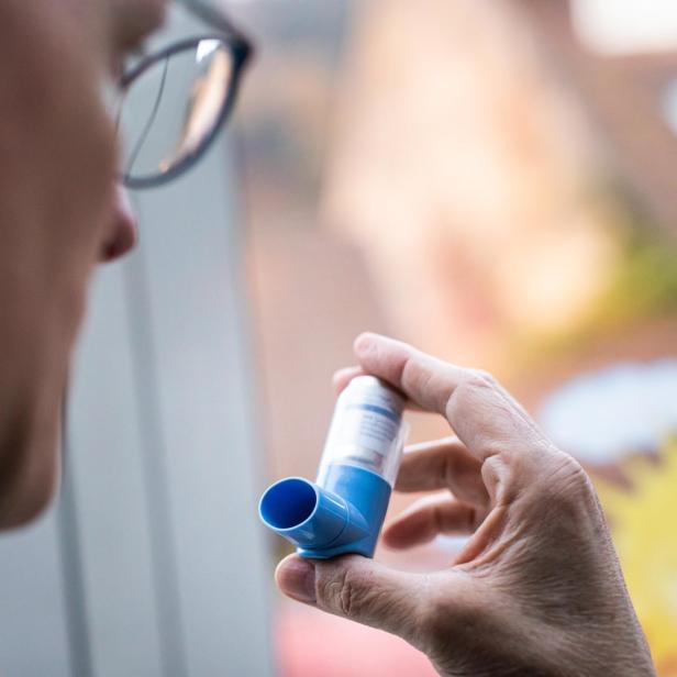 Ein Mann mit Brille betrachtet einen blauen Asthmainhalator.