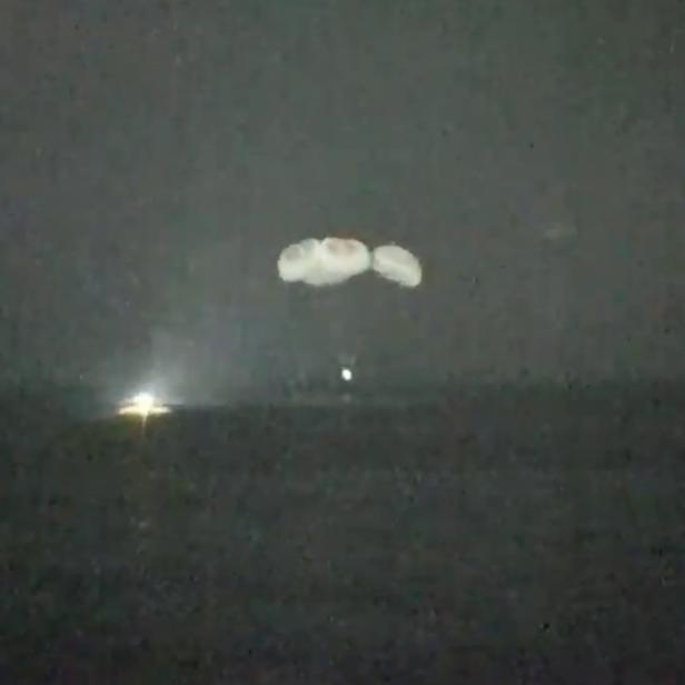 Mehrere Fallschirme schweben während einer NASA-Liveübertragung in der Dunkelheit herab.