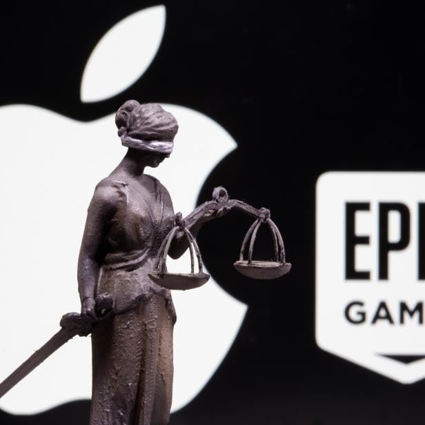 3D printed Lady Justice figure is seen in front of displayed Apple and Epic Games logos in this illustration photo