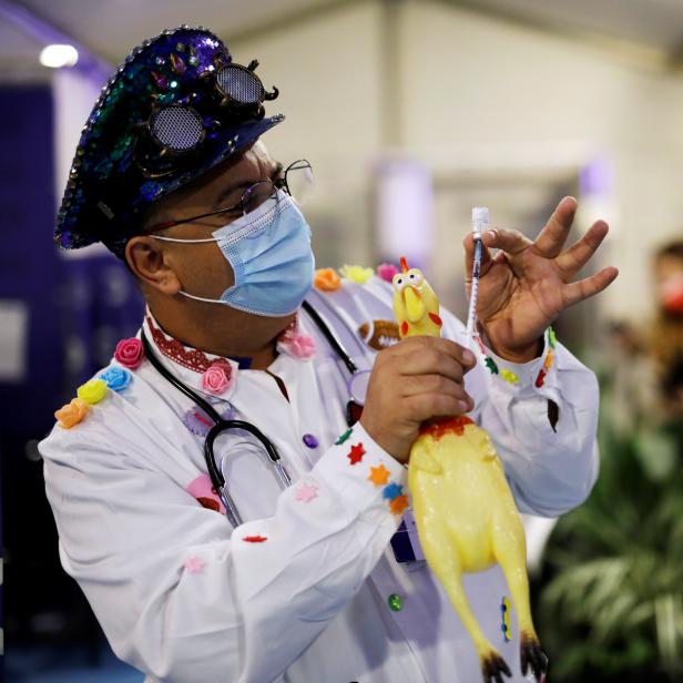 A medical clown holds a toy chicken, syringe and vial as he performs at a temporary Clalit healthcare maintenance organisation (HMO) centre, where vaccinations against the coronavirus disease (COVID-19) are administered, in Herzliya