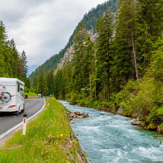 Camper van with attached bicycle driving through the European Alps on a rainy day