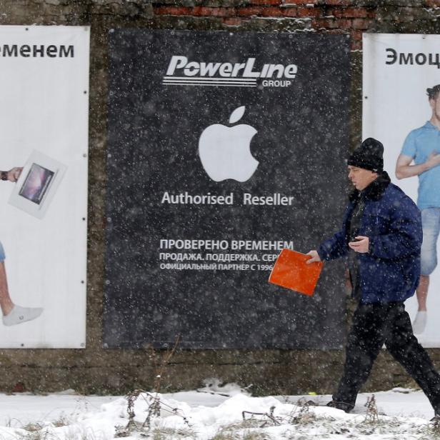 Ein Mann geht an Werbetafeln für Apple und PowerLine vorbei, während es schneit.
