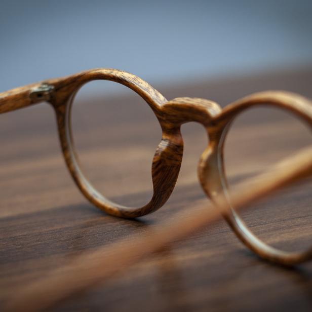 Eine hölzerne Brille liegt auf einem dunklen Holztisch.