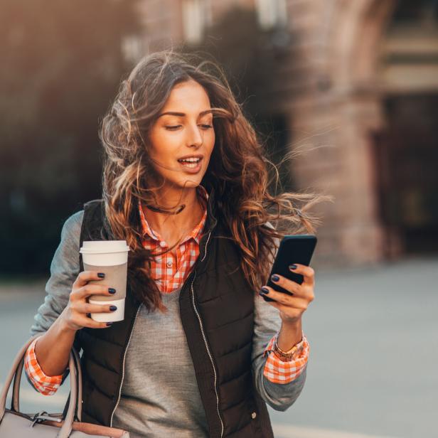 Woman texting and drinking coffee outdoors.