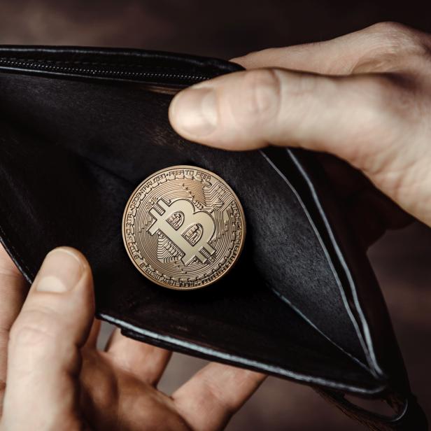 Eine Bitcoin-Münze liegt in einem leeren, schwarzen Portemonnaie.