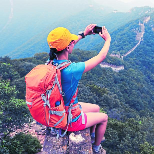 young woman hiker taking photo with smart phone on top of great wall