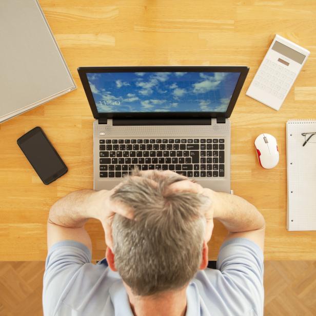 Stressed man sitting at a table with laptop while working from home - view from above