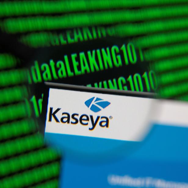 Kaseya's webpage is seen through magnifying glass in front of displayed binary code
