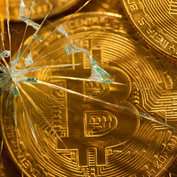 Representations of virtual currency bitcoin are seen through broken glass in this illustration