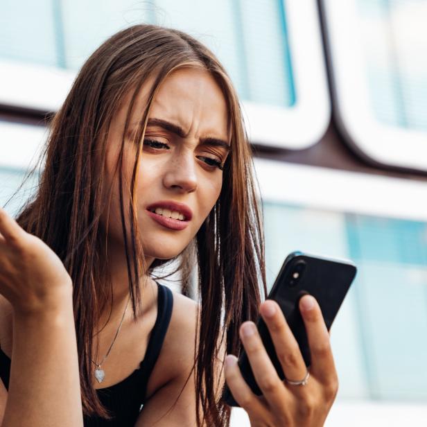 Eine junge Frau schaut verärgert auf ihr Smartphone.