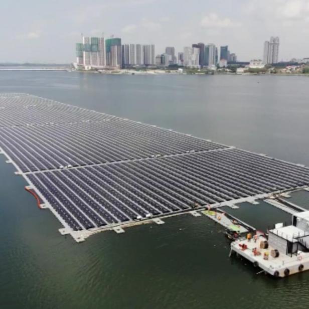 Eine schwimmende Solaranlage auf einem See vor einer Stadtkulisse.