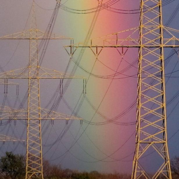 Ein Regenbogen erstreckt sich hinter einer Reihe von Strommasten.