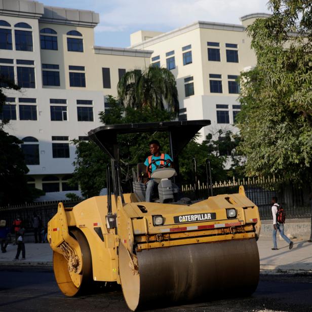 A worker drives a steamroller, with the new building for the Ministry of Economy and Finance in the background, in Port-au-Prince