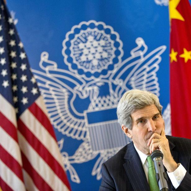 John Kerry spricht vor US-amerikanischer und chinesischer Flagge.
