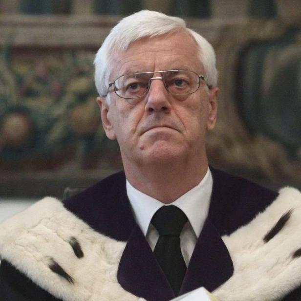 Ein Mann mit Brille und weißem Haar trägt eine Robe mit Fellbesatz.