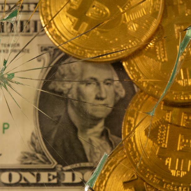Dollar and bitcoin are pictured through broken glass in this illustration