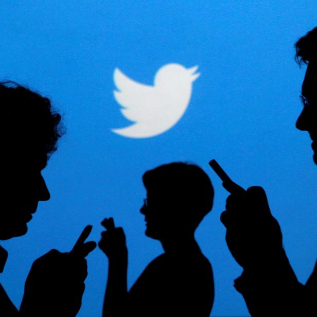 FILE PHOTO: FILE PHOTO: People holding mobile phones are silhouetted against a backdrop projected with the Twitter logo  in Warsaw