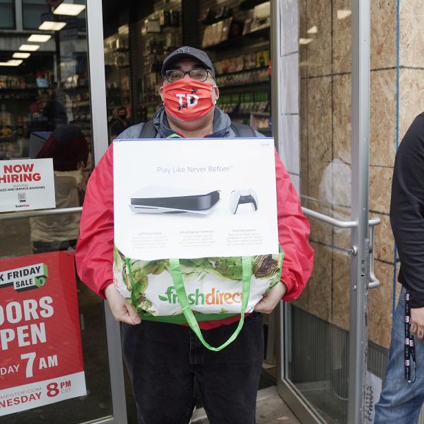 A man poses outside a GameStop store with his purchase of a Sony PS5 gaming console