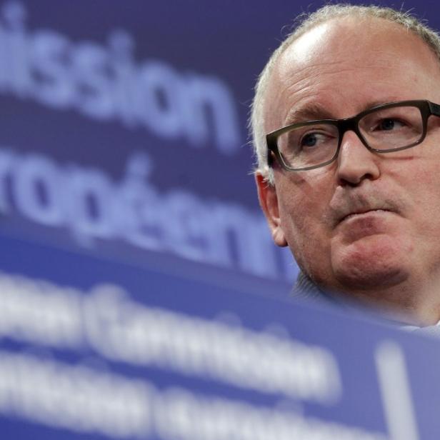Ein Mann mit Brille steht vor einem Schild der Europäischen Kommission.