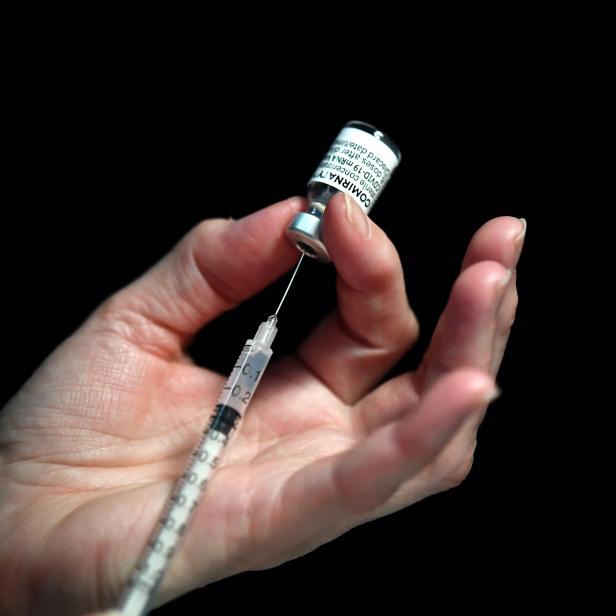 Eine Hand zieht eine Dosis des Comirnaty COVID-19-Impfstoffs in eine Spritze.