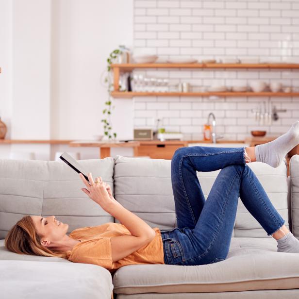 Woman Relaxing Lying On Sofa At Home Looking At Digital Tablet