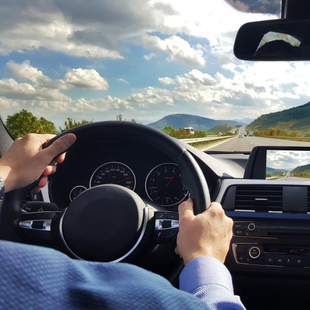 Blick aus dem Inneren eines Autos auf eine Autobahn mit Bergen im Hintergrund.