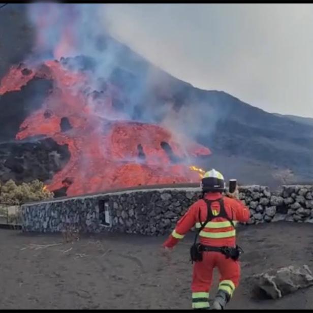 Ein Feuerwehrmann beobachtet einen Lavastrom an einem Berghang.