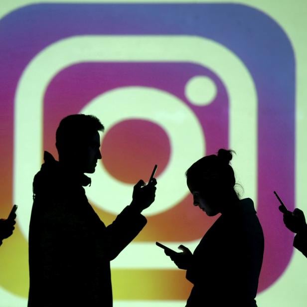 FILE PHOTO: Silhouettes of mobile users are seen next to a screen projection of Instagram logo in this picture illustration