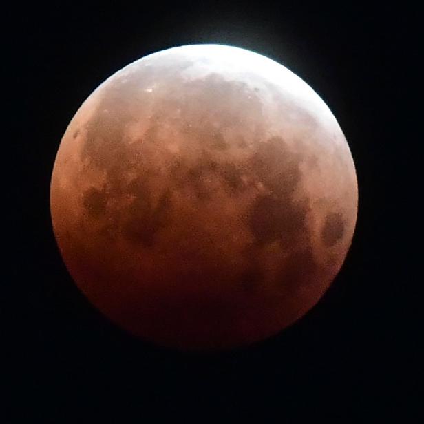 Eine totale Mondfinsternis leuchtet rot am Nachthimmel.