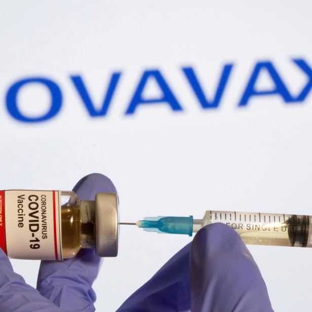 FILE PHOTO: FILE PHOTO: A woman holds a small bottle labeled with a "Coronavirus COVID-19 Vaccine" sticker and a medical syringe in front of displayed Novavax logo in this illustration