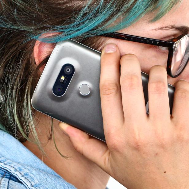 Eine Frau mit Brille telefoniert mit einem grauen Smartphone.