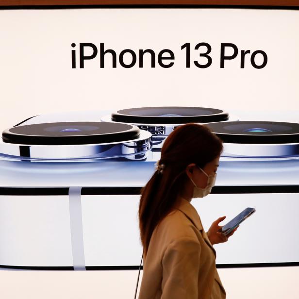 FILE PHOTO: A woman wearing a face mask walks past an image of an iPhone 13 Pro at an Apple Store in Beijing