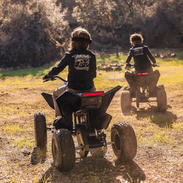 Zwei Kinder fahren mit Quads durch eine ländliche Gegend.