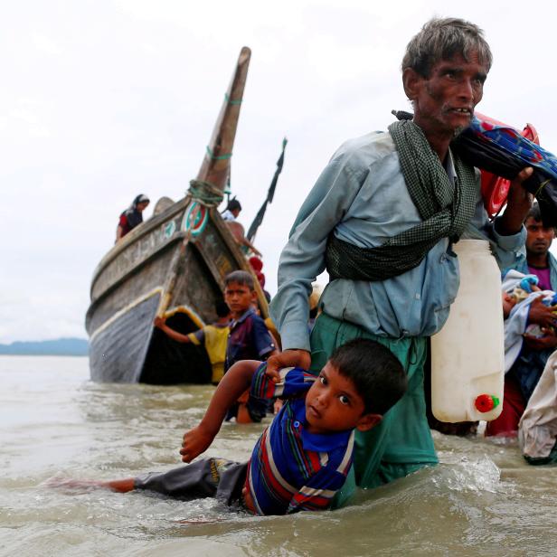 FILE PHOTO: A Rohingya refugee man pulls a child as they walk to the shore after crossing the Bangladesh-Myanmar border by boat through the Bay of Bengal in Shah Porir Dwip